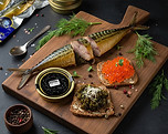 Smoked fish with caviar and appetizers on a wooden serving board.