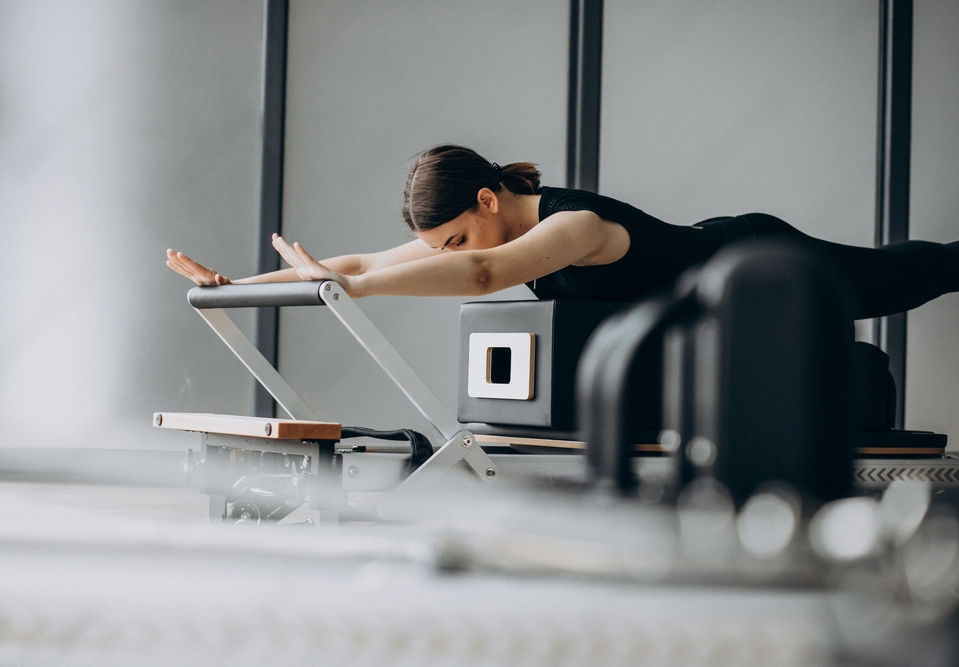 Image of a woman with brown hair taking part in Reformer Pilates wearing black.