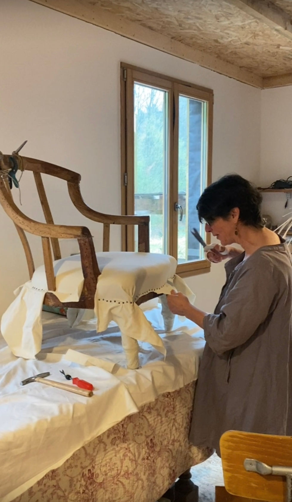 mage montrant un fauteuil en cours de retapissage avec pose de semences par un artisan tapissier, illustrant la restauration d’un siège ancien plutôt que l’achat d’un meuble neuf.