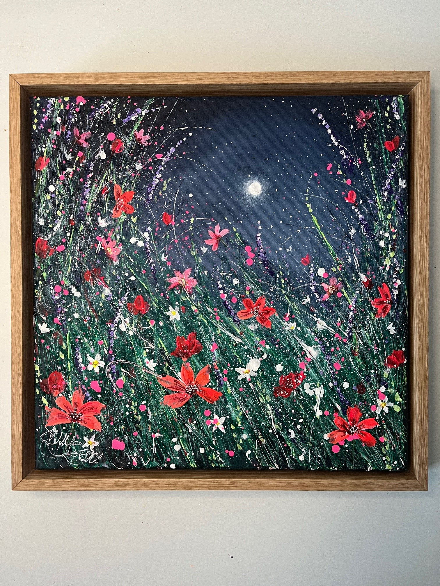 Canvas framed in oak and painted a dark blue sky with glowing moon. Energetic green grass is scattered with pink wildflowers
