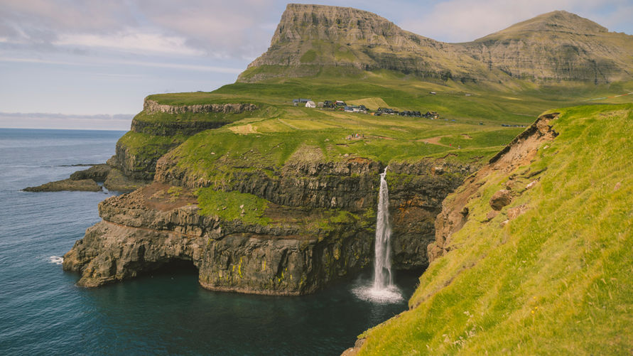 Múlafossur waterfall falls into the ocean beneath Gásadalur village and green mountains.