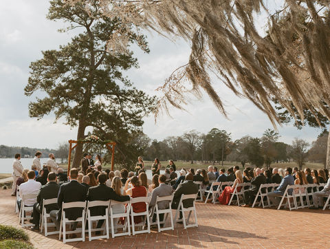 a wedding ceremony in front of a lake with Spanish moss hanging overhead