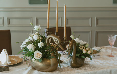 two brass swans filled with flower at the head table of a wedding