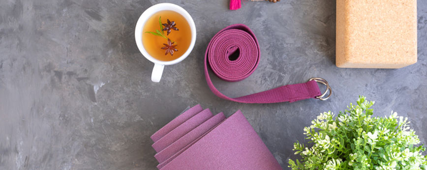 Yogamatte, Yogablock, Yogagurt, Meditationskette, Tee mit Blüten und eine grüne Pflanze dekorativ platziert