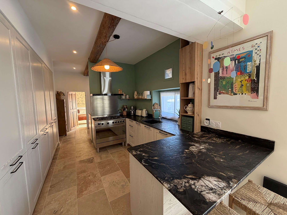 Cuisine moderne avec un comptoir noir élégant, peinture colorée au mur, plafond en poutres apparentes. Éclairage chaleureux, ambiance cosy. Rénovation a Nimes