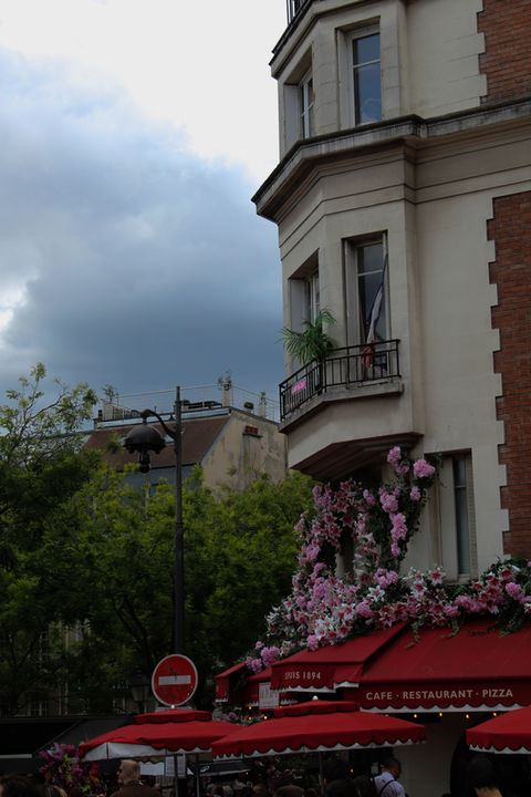 A white building with black balconies, pink flowers, and a red awning