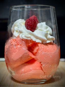 Glass bowl of fluffy pink keto Jello whip topped with sugar-free whipped cream and a fresh raspberry.
