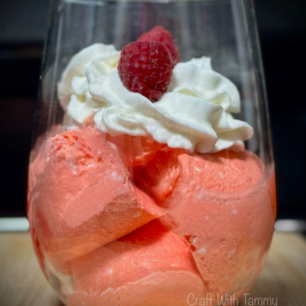 Glass bowl of fluffy pink keto Jello whip topped with sugar-free whipped cream and a fresh raspberry.