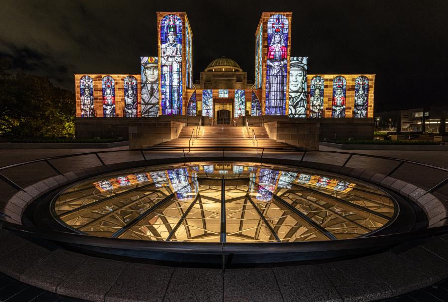 Australian War Memorial Museum lit up showing faces of soldiers on the walls outside.