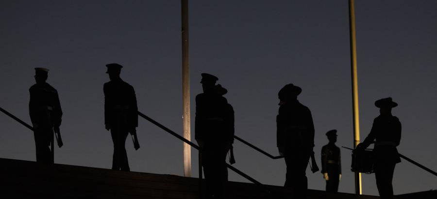 Anzac soldiers at a pre dawn service under flag poles