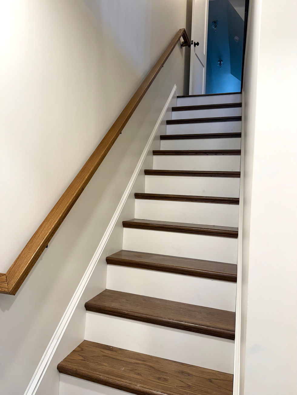 Modern staircase with dark wood steps contrasted with white trim and a natural oak railing.