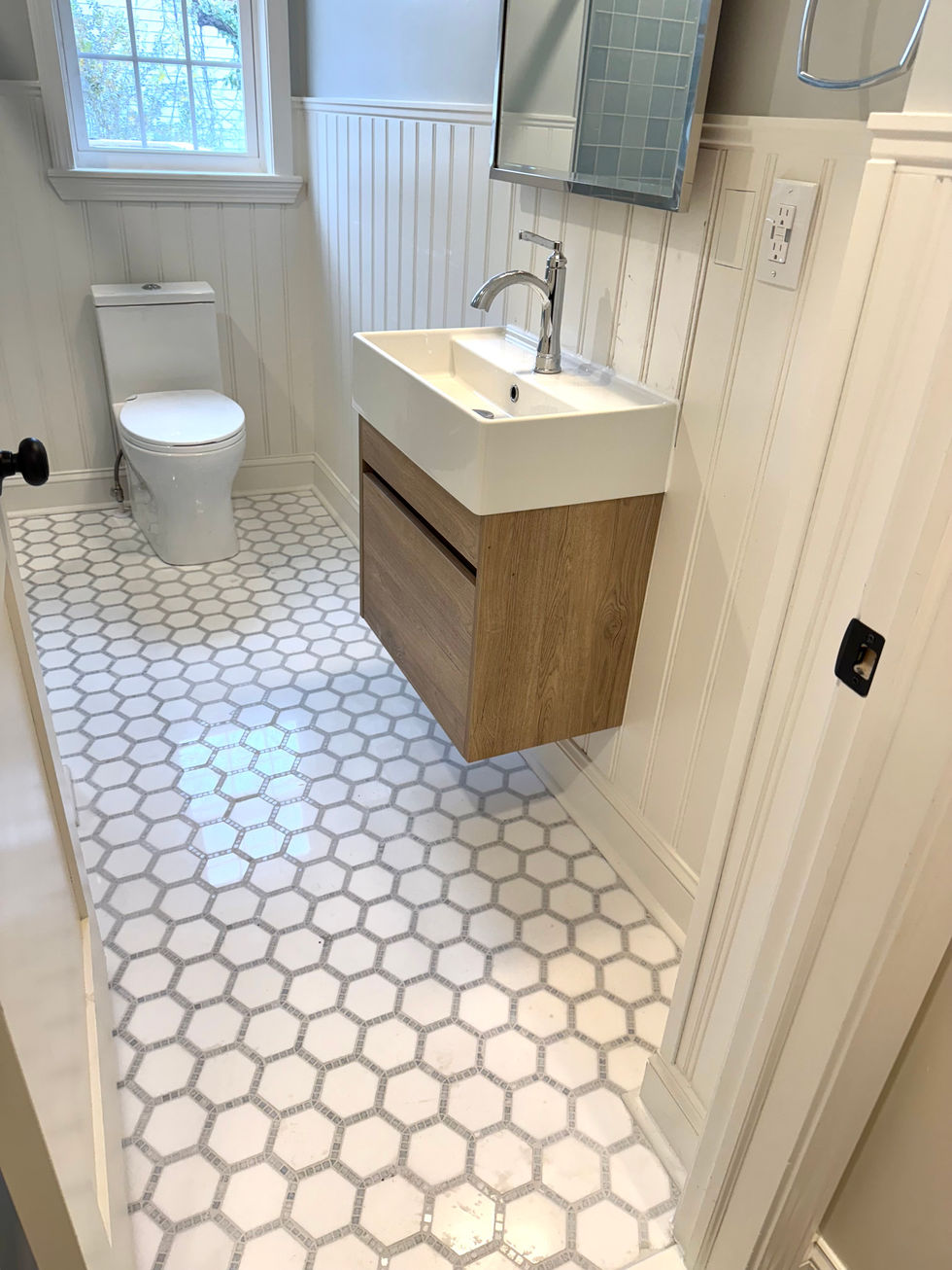 Modern bathroom with a wood floating vanity and white-and-grey hexagonal floor tiles.