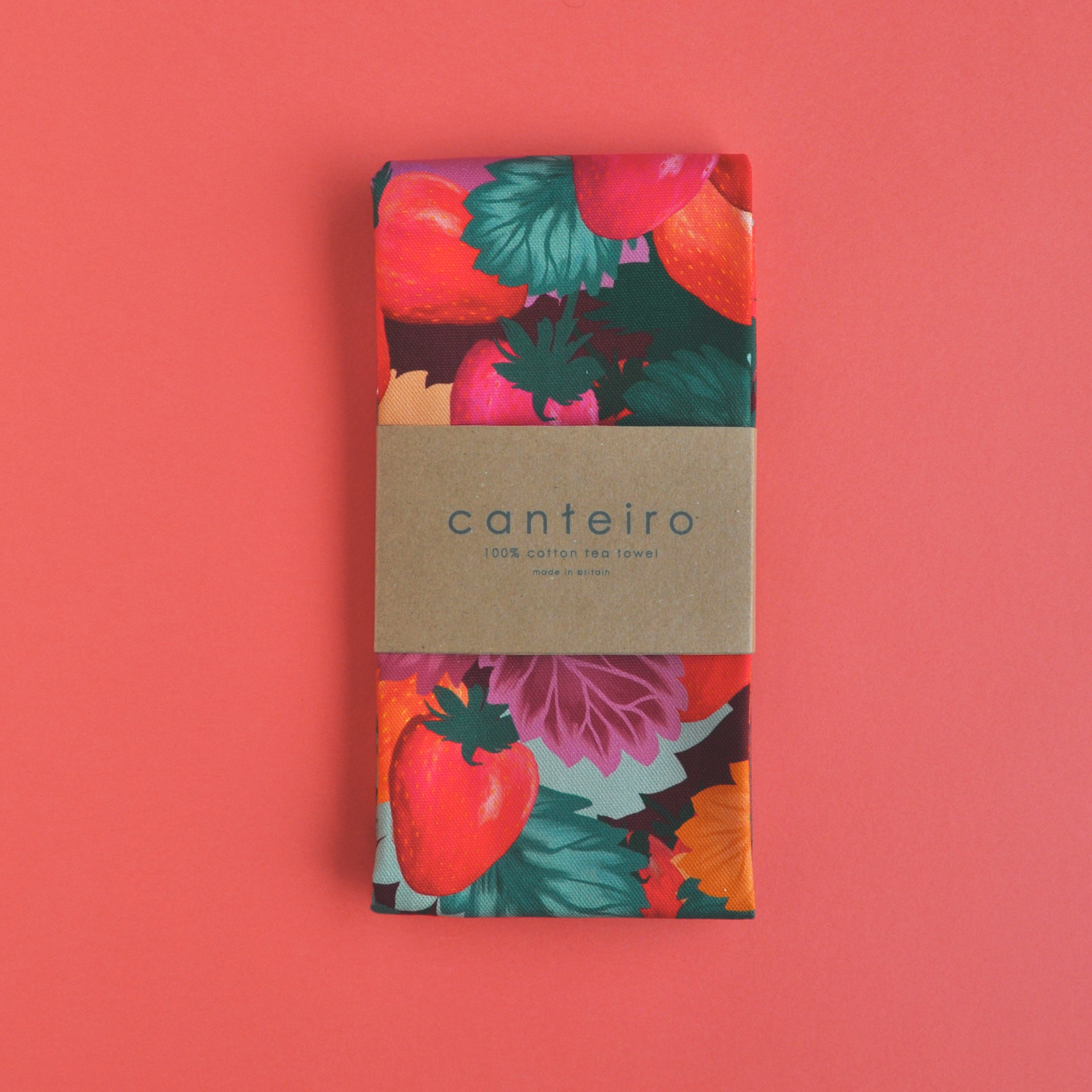 An image of a folded printed tea towel, with red and green strawberry print