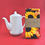 Thumbnail: A still life image of a folded printed tea towel, with a black and yellow sunflower print