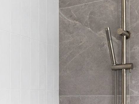 Silver rain shower and handheld head on grey and white tiled bathroom wall.