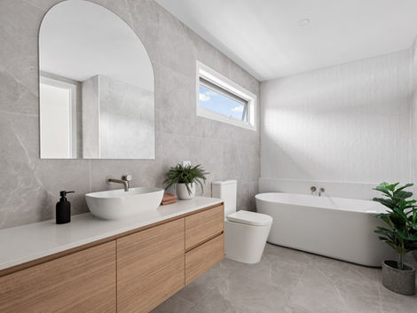 Bathroom with floating timber vanity, curved mirror, white bath and grey tiled walls.