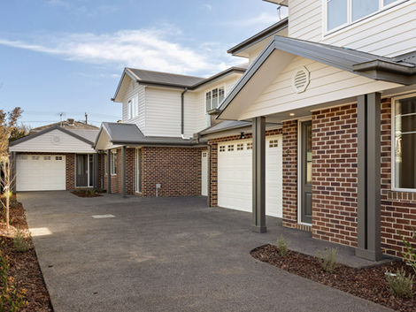 Brick townhouse facades with white garage doors and asphalt driveway under a clear sky.