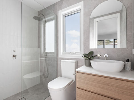 Ensuite bathroom with timber vanity, white basin, walk-in shower, and arched mirror.