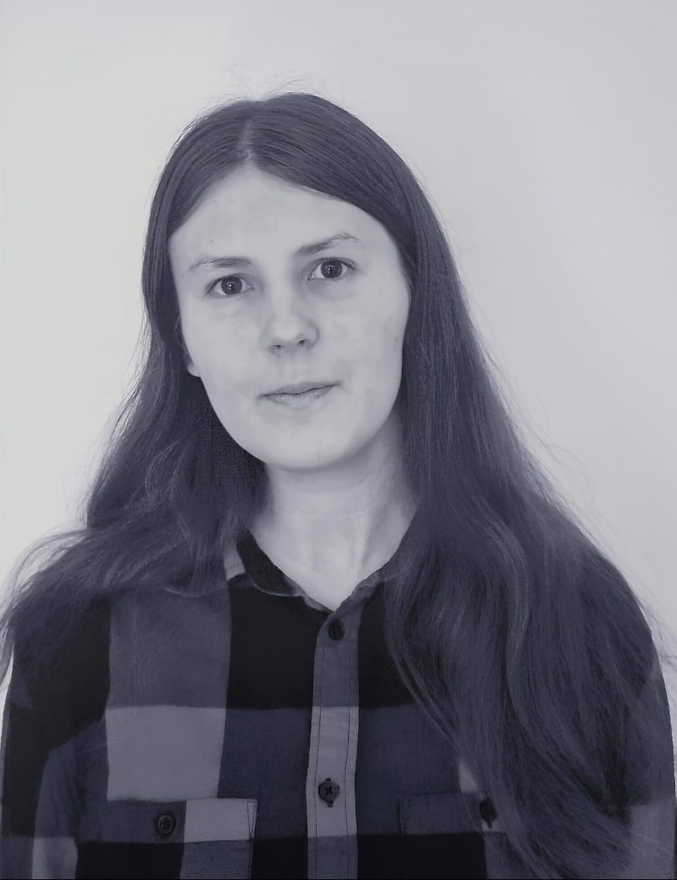 Portrait of a woman with long dark hair in a black-and-gray plaid shirt against a plain light background, looking calmly at camera
