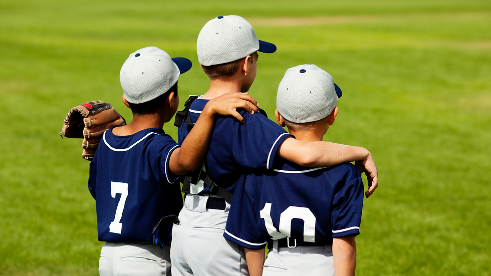 Three boys in baseball uniforms with arms around each other, standing on a grassy field.