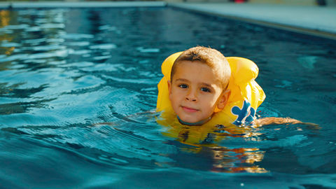Young boy smiling in a domestic pre fabricated ecological pool with clear water.