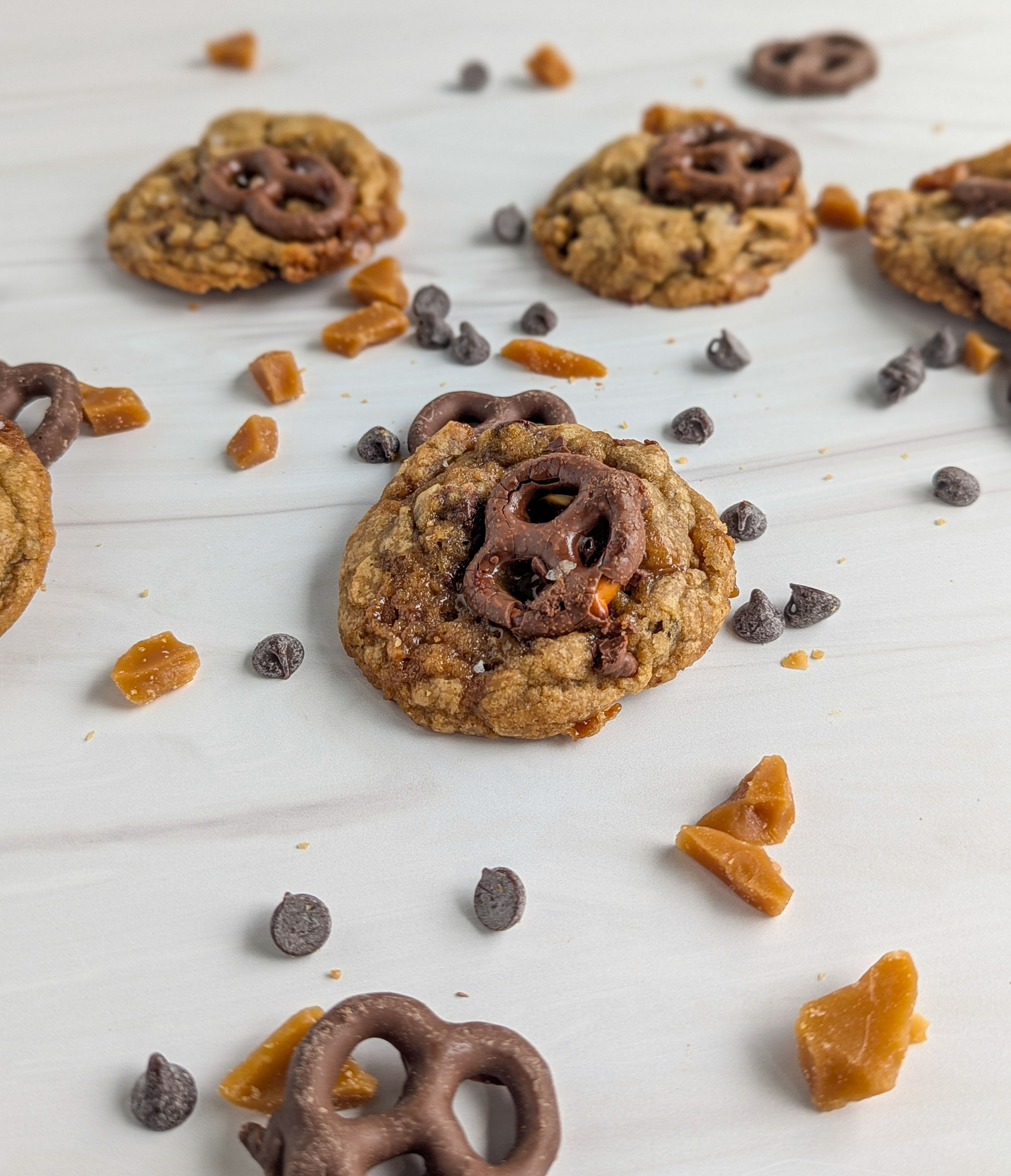 kitchen sink cookies with chocolate covered pretzel in their center. chocolate chips and toffee pieces surround the cookies.