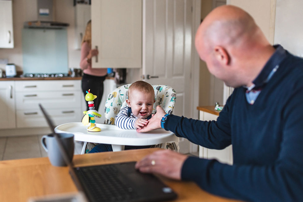 Authentic home shot with young father working from home and playing with his newborn baby