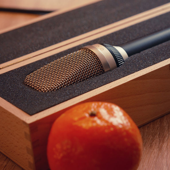 Foto eines Vintage-Mikrofons im geöffneten Holz-Case auf einem Studiotisch. Davor liegt provokativ eine reife Mandarine als kreativer Kontrast zur technischen Studioszenerie.