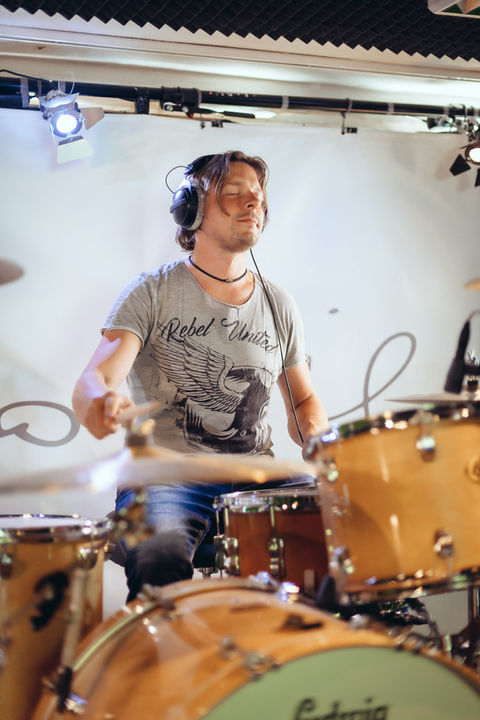 Foto eines Schlagzeugers mit geschlossenen Augen während einer Studioaufnahme. Er spielt verträumt an einem vollständig mikrofonierten Schlagzeug und nimmt einen Drum-Take im Tonstudio auf.