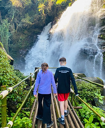 Travelers walking across a bridge toward a waterfall in Doi Inthanon National Park, Chiang Mai.