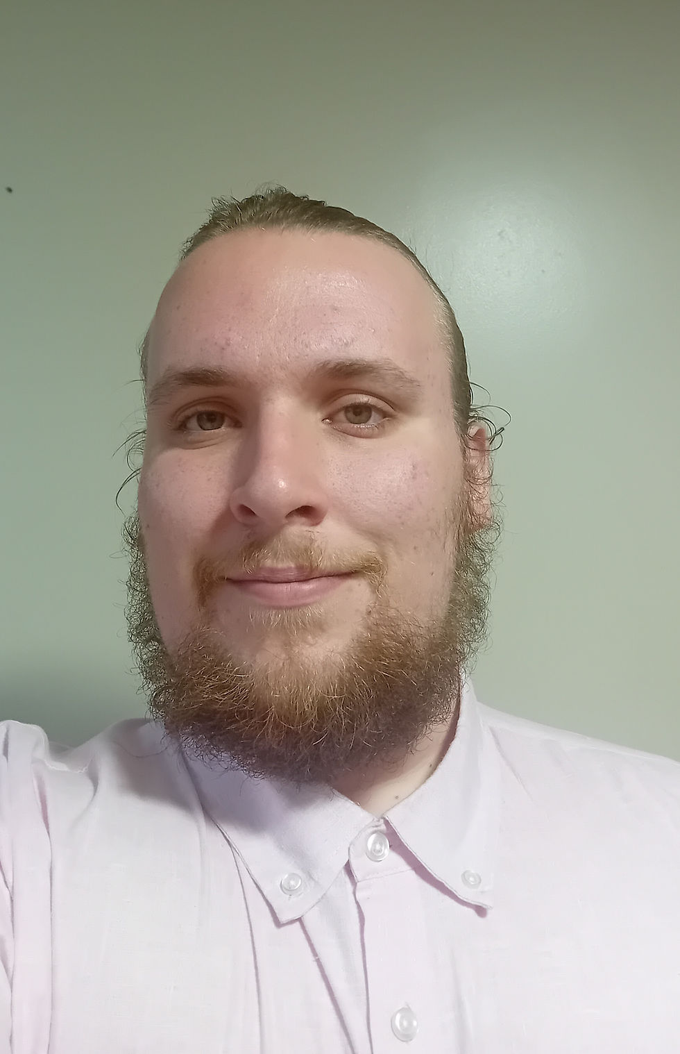 Man with a light brown beard smiling in a white shirt (Alfie Exton- emollient PhD researcher)