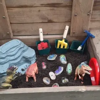 a container with mud, spades and small animals in nursery garden
