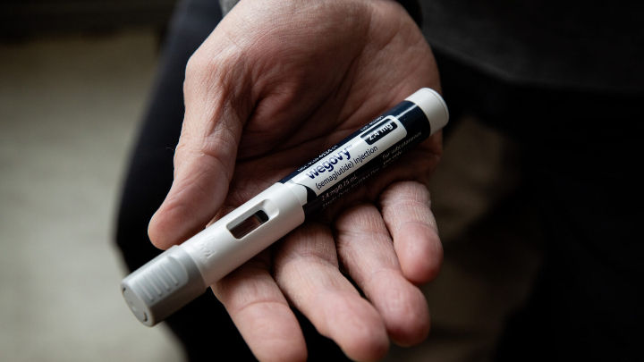 Una persona sostiene un autoinyector de semaglutida, una pluma de medicación llamada "Wegovy". La mano está desenfocada, pero la pluma está enfocada en el centro.