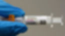 A blue-gloved hand holds a Comirnaty (COVID-19) vaccine syringe, 2024-2025 formula. The label specifies a 0.3 ml dose for ages 12+, emphasizing current immunological prevention.
