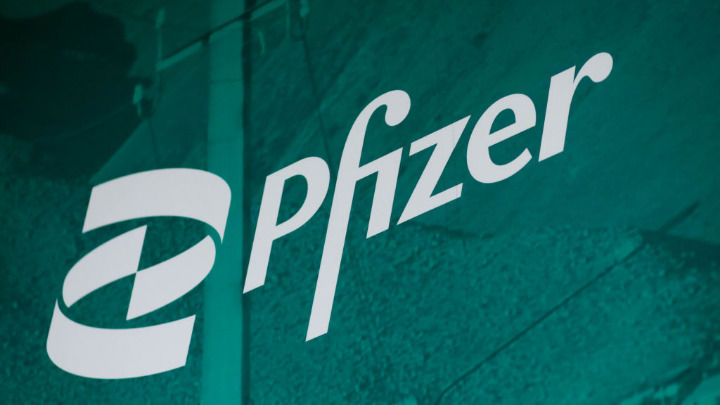 The white and blue Pfizer logo is displayed diagonally in the foreground against a dark teal, textured background, creating a professional and corporate medical aesthetic.
