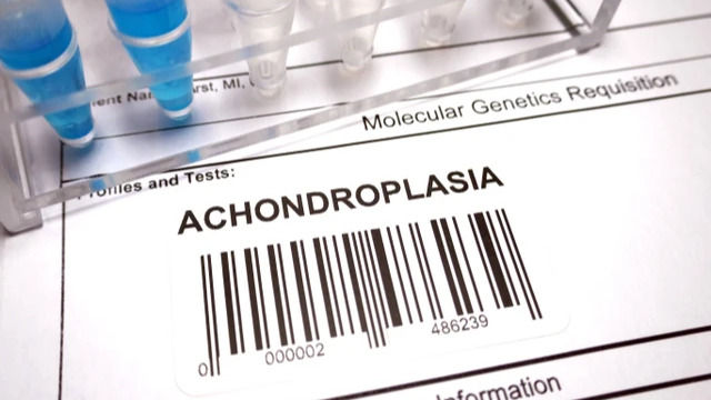 Formulario médico de "Molecular Genetics Requisition" con la palabra "ACHONDROPLASIA" y tubos de ensayo con líquido azul.