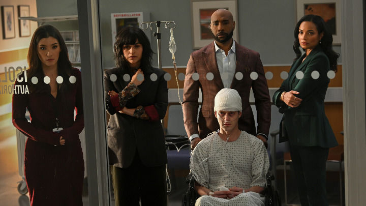 This scene shows Dr. Watson and three colleagues with serious expressions standing behind a patient in a wheelchair with a bandaged head, looking through a glass door in a professional hospital setting.