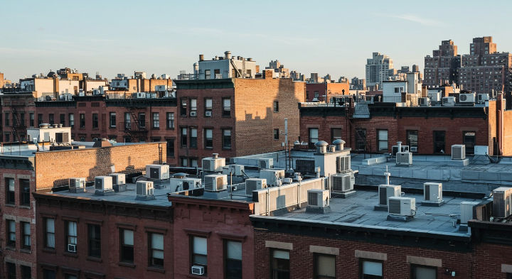Una vista detallada de las azoteas de los edificios de ladrillo de la ciudad de Nueva York, con numerosos aires acondicionados. El sol de la tarde ilumina las fachadas de los edificios.
