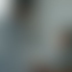 A smiling male doctor in a white coat leans over a hospital bed, talking to an elderly female patient. He is holding her hand, creating a reassuring atmosphere.