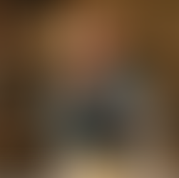 An elderly man in a blue shirt stands in a kitchen, holding a yellow capsule and a glass of water, with a bottle of Centram Silver vitamins on the table beside his breakfast.