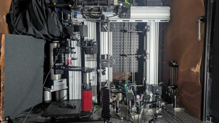 A complex, dense setup of scientific equipment and optical components is mounted on an aluminum frame inside a laboratory chamber, likely for advanced imaging.