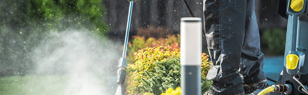 Worker pressure washing lawn, cleaning home exterior