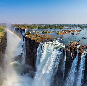 Espectacular cascada que cae sobre acantilados rocosos con un vibrante arcoíris en el cielo.