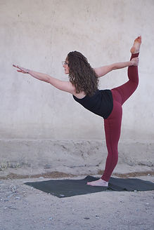 white female yoga teacher in dancers pose standing bow pulling pose with gray stone background