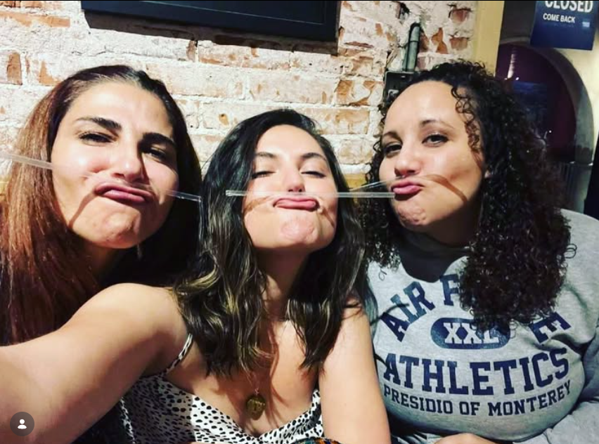 Three women make duck-face selfie in a brick-walled bar; CLOSED COME BACK sign visible in the background.
