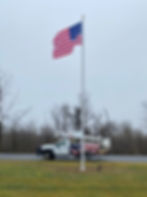 Tall internal halyard commercial flagpole with an American flag, featuring a lockable access door and winch-operated stainless steel cable system.