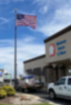 Tall internal halyard commercial flagpole with an American flag, featuring a lockable access door and winch-operated stainless steel cable system outside Windows Doors and More in Fort Wayne