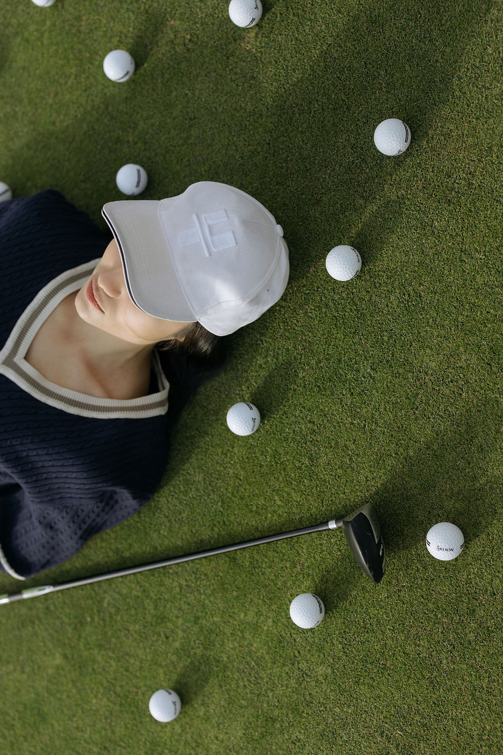 Girl laying on a golf course green surrounded by golf balls, representing Markateing’s creative photography and videography services for lifestyle and outdoor brands.