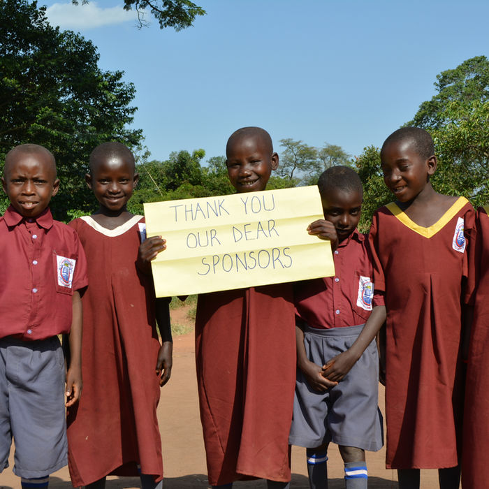 Group of school children holding sign: Thank You Our Dear Sponsors. Uganda Schools.