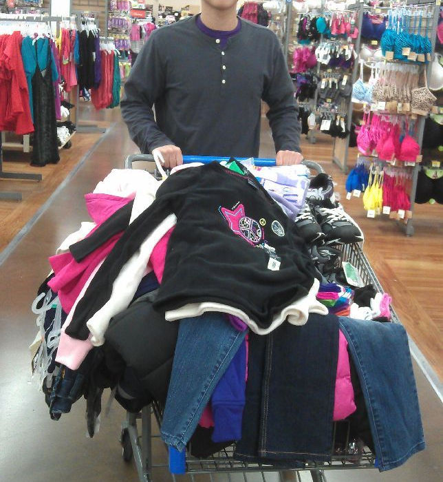 Man pushing shopping cart full of clothes in Walmart store.